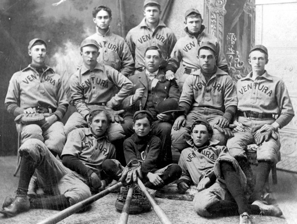 Antique photo of nine baseball players, one coach and a mascot.