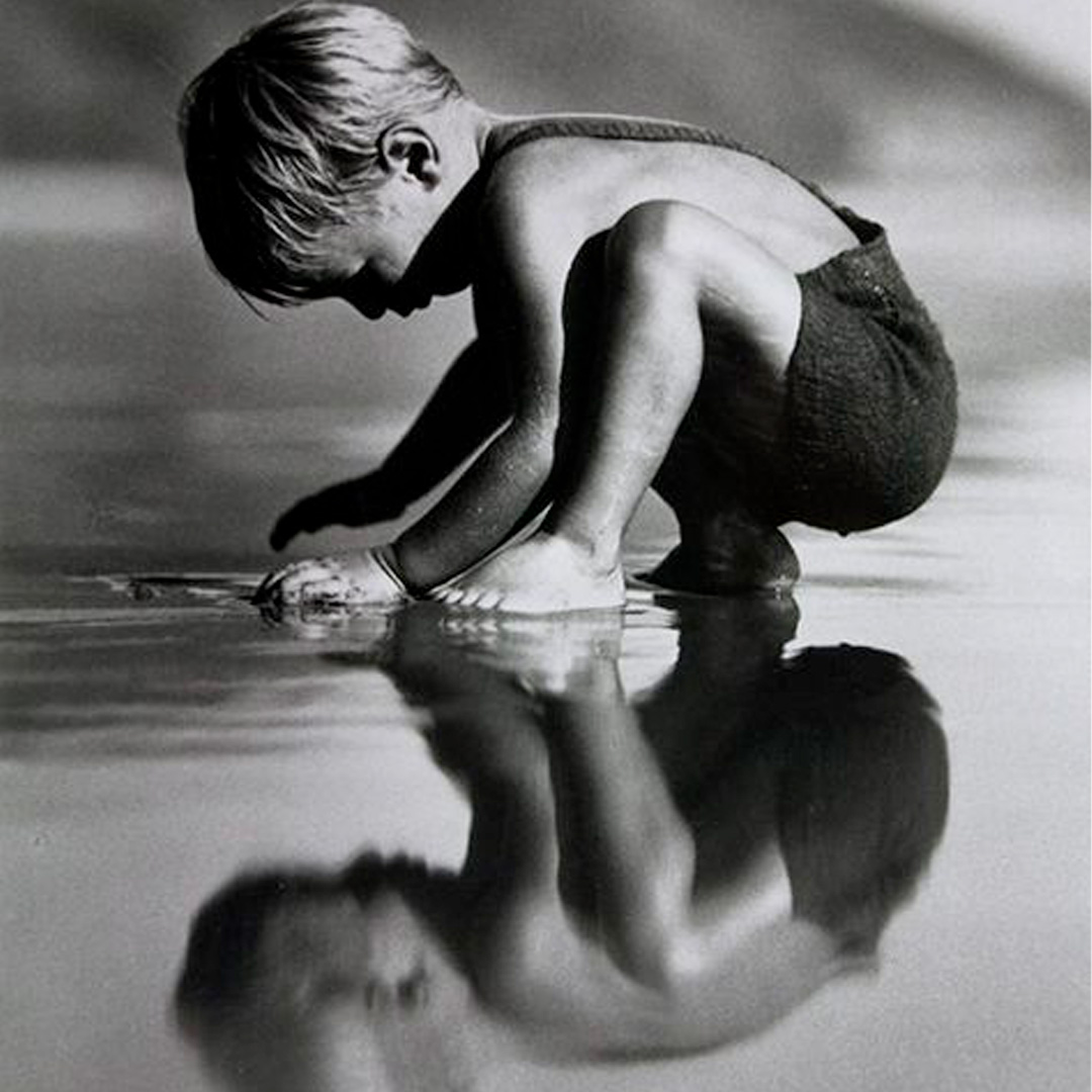 Photo of child looking at reflection on beach